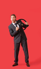 Obraz premium Young businessman with steering wheel on color background