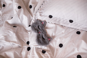 a gray plush sleep mask lies on the cotton bed linen on the bed