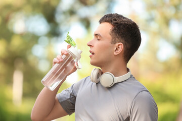 Obraz premium Sporty young man drinking water after running in park