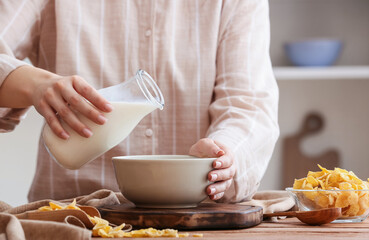 Woman pouring milk from bottle to bowl on wooden table