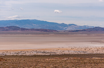 Fototapeta na wymiar High Desert, Nevada, USA - May 17, 2011: Wide landscape with flat beige colored dry lake with mountain range in back under gray cloudscape..