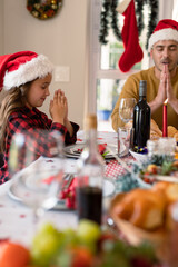 Caucasian daughter and father wearing santa hats praying at christmas table