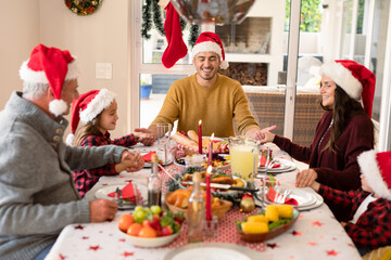 Caucasian multi generation family wearing santa hats praying at christmas table