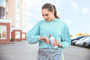 Sporty young woman with bottle of water and fitness tracker outdoors