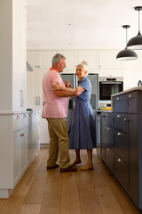 Happy caucasian senior couple dancing together in kitchen and having fun