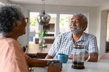 Happy african american senior couple sitting in kitchen with coffee and talking - Powered by Adobe