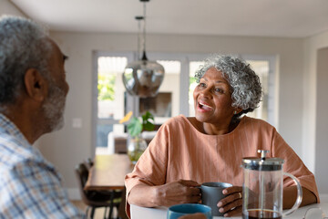 Happy african american senior couple sitting in kitchen with coffee and talking