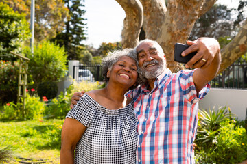 Happy african american senior couple taking selfie in garden