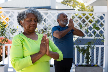 Focused african american senior couple practicing yoga in garden