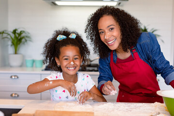 Happy african american mother and daughter baking together in kitchen