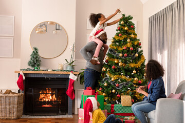 Happy african american parents and daughter decorating christmas tree - Powered by Adobe