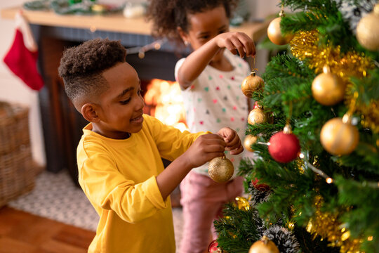 Happy african american siblings hanging baubles, decorating christmas tree