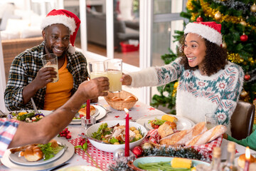 Happy african american couple wearing santa hats, making toast at christmas table