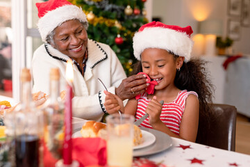 Happy african american grandmother cleaning granddaughter face at christmas table