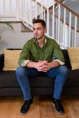 Thoughtful caucasian man sitting on sofa and looking at camera