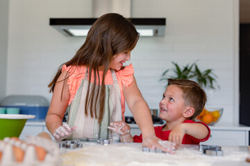 Happy caucasian siblings baking together, making cookies in kitchen