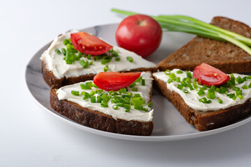Slices of bread with cottage cheese, onion and tomatoes on plate on white background