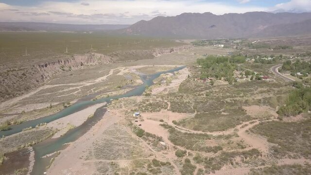 Aerial view of river, desert vegetation and mountains in the background.