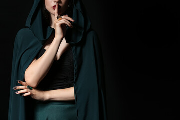 Young witch showing silence gesture on dark background