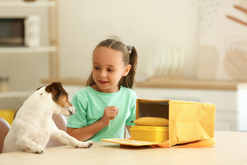 Fototapeta na wymiar Cute little girl with funny dog putting her lunch in bag