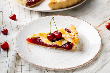 Plate with piece of tasty cherry pie on light wooden background, closeup
