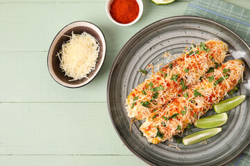 Plate with tasty Elote Mexican Street Corn, cheese and pepper on green wooden background