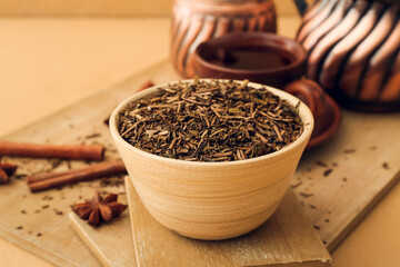 Board with dry hojicha green tea and cup of hot beverage on color background