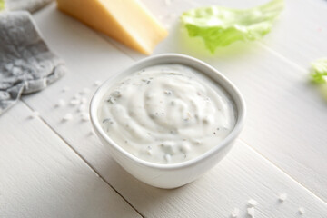 Bowl of tasty Caesar sauce on white wooden background