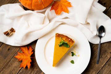 a piece of American pumpkin pie on a white plate and a wooden table