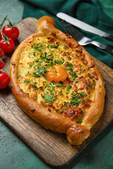 Wooden board with tasty Ajarian khachapuri on color background