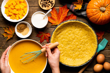 the process of making American pumpkin pie women's hands on a wooden table with ingredients, autumn food composition