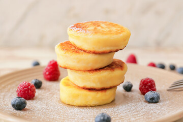 Plate with cottage cheese pancakes and berries on light wooden background