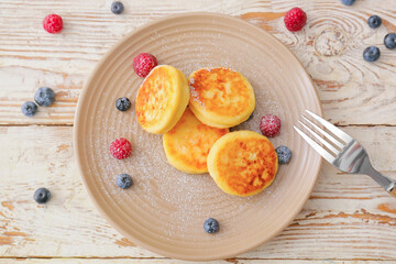 Plate with cottage cheese pancakes and berries on light wooden background
