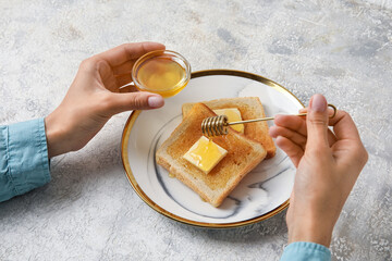 Woman preparing tasty toasted bread with honey on light background