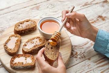 Woman preparing tasty toasted bread with honey on white wooden background