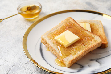 Plate of tasty toasted bread with honey and butter on table