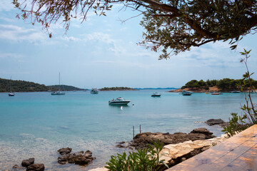 Boats moored in a calm bay, view from the beach bar through vegetation, on Kosirina beach, Murter island, Croatia