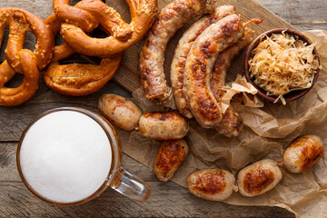 Mug of cold beer, board with Bavarian sausages and snacks on wooden background. Oktoberfest celebration