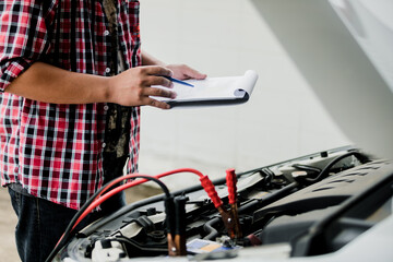 Close up of automotive mechanics checking engine room with jumping leads for jump starting...