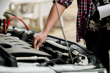 Fototapeta na wymiar Close up of automotive mechanics checking engine room with jumping leads for jump starting automotive batteries in the garage, battery booster cables, auto maintenance service concept.