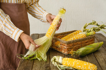 Woman peeling corn cob on wooden table