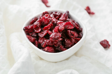 Bowl with tasty dried cranberries on fabric background, closeup