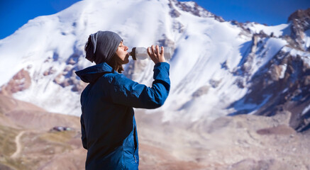 Young girl drinks water in the mountains.