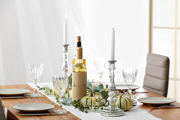 Beautiful table serving with autumn decor, bottles of wine and candles in light room