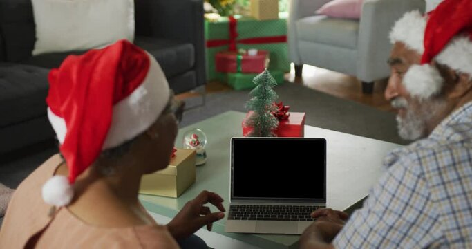 Animation of african american senior couple using laptop with copy space on screen at christmas time