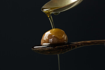 Extra virgin olive oil flows on a wooden spoon full of green olives against black background.	