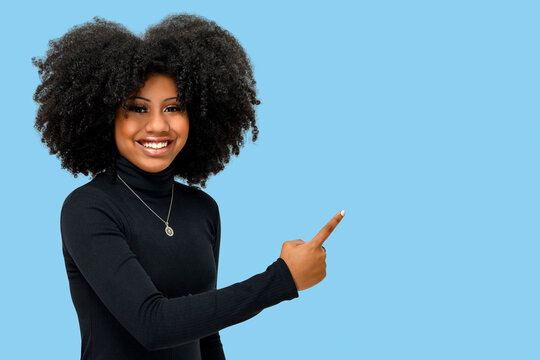 portrait of a smiling young afro girl points to the rigth side isolated on a blue background
