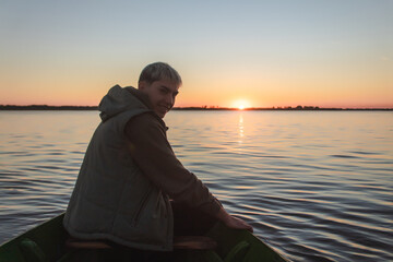 Young smiling man sailing in a small boat on the sea at sunset.