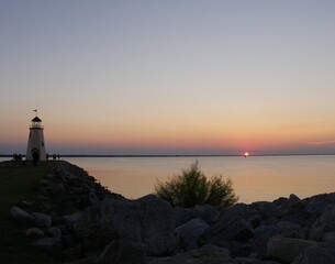 Lighthouse view with a sunset reflected in the lake, with silhouttes of people