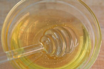  Liquid honey in transparent glass jar with dipper.Glass stick for honey in a glass cup on a wooden table. Organic Fresh honey. 